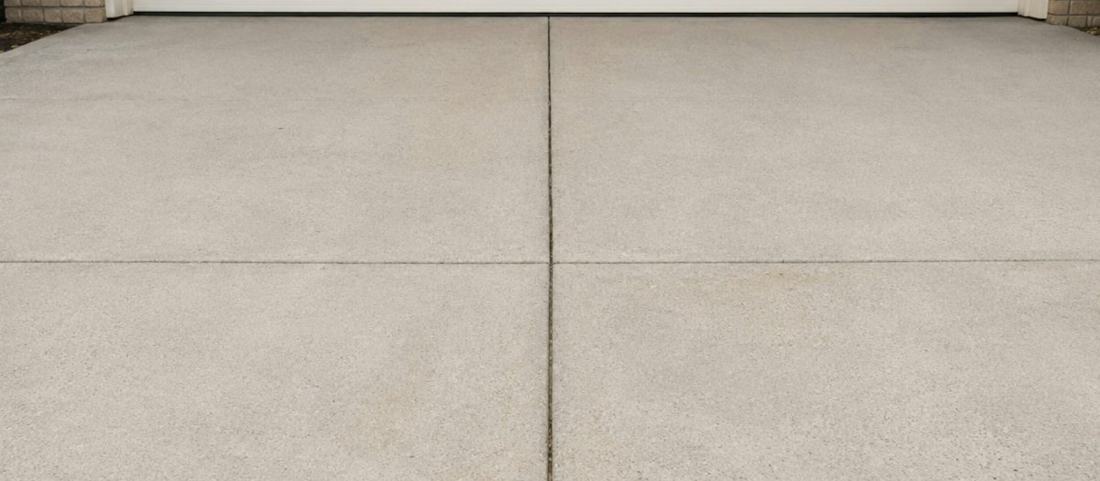 A freshly finished plain concrete driveway in front of a double garage